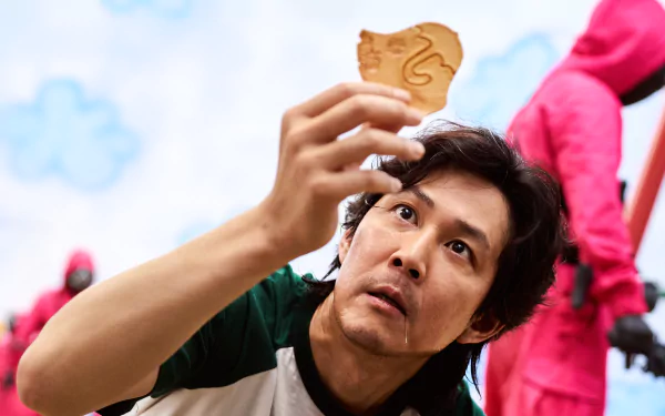 Seong Gi-Hun from the TV show Squid Game examines a cookie, featured in a 4K Ultra HD desktop wallpaper with Lee Jung-jae in the background.