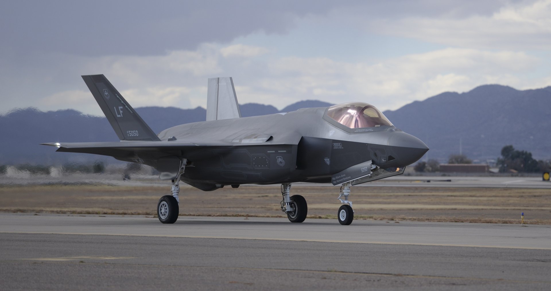 Lockheed Martin F-35 Lightning II warplane jet fighter on a runway with mountain backdrop — military stealth aircraft, 4K Ultra HD PC desktop wallpaper.