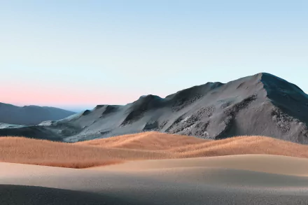 HD desktop wallpaper of a serene desert scene with rolling sand dunes and rugged mountains, set against a clear blue sky.