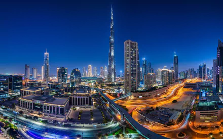 Nighttime Dubai skyline with the Burj Khalifa towering above illuminated skyscrapers and winding highways — man-made cityscape in the United Arab Emirates, 2K Quad HD PC desktop wallpaper.