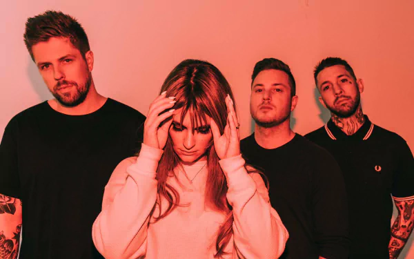 HD wallpaper featuring a music group with a female member front and center, touching her temples, surrounded by three male members against a red background, tagged with Spiritbox.