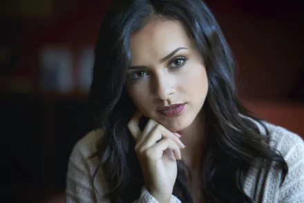 HD PC desktop wallpaper of a black-haired woman model gazing into the camera, hand near her chin, soft lighting and a blurred background.