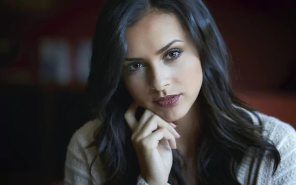 HD PC desktop wallpaper of a black-haired woman model gazing into the camera, hand near her chin, soft lighting and a blurred background.