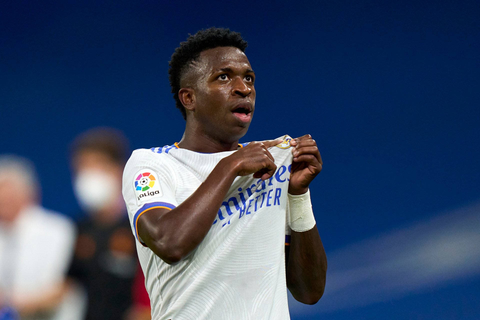 2K Quad HD PC desktop wallpaper: professional soccer player in a white kit clutching his jersey on the pitch, focused expression, blurred stadium background.