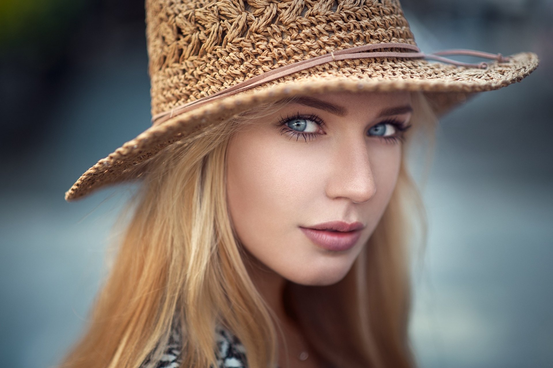 HD desktop wallpaper: close-up portrait of a blonde woman with striking blue eyes wearing a woven straw hat, soft-focus background.