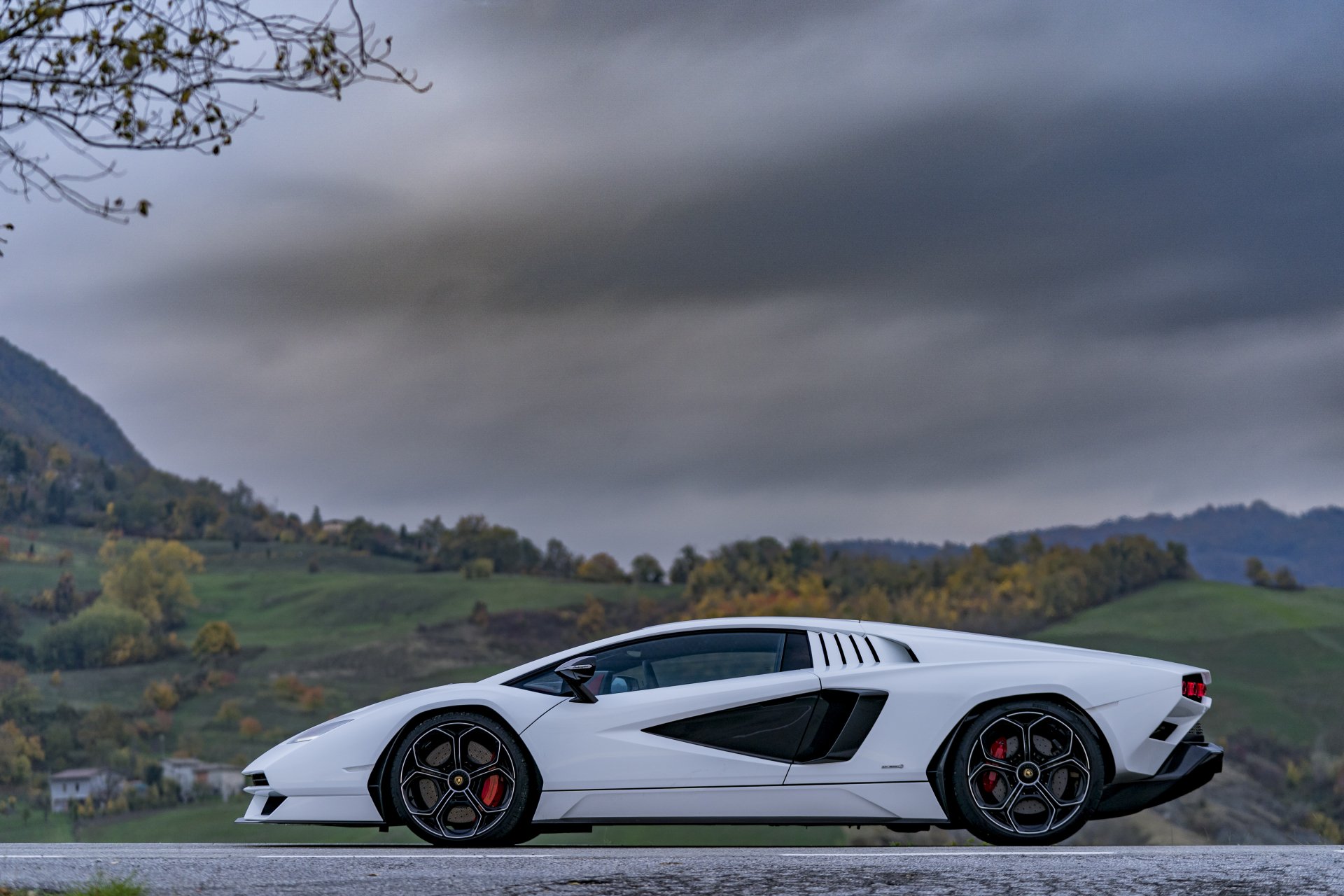 White Lamborghini Countach LPI 800-4 supercar vehicle, side profile on a road with rolling green hills under a dramatic cloudy sky — 5K Ultra HD PC desktop wallpaper background