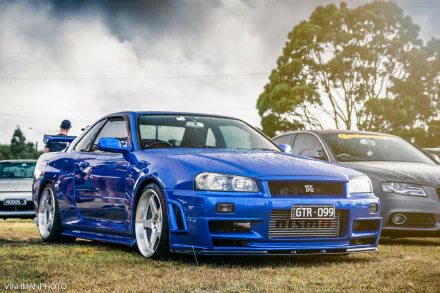 Blue Nissan Skyline R34 parked outdoors with a subtle smoky background, showcased as a high-definition desktop wallpaper.