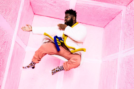 A person in vibrant clothing jumps against a pink geometric background. HD desktop wallpaper with a tag 'Pink Sweats'.