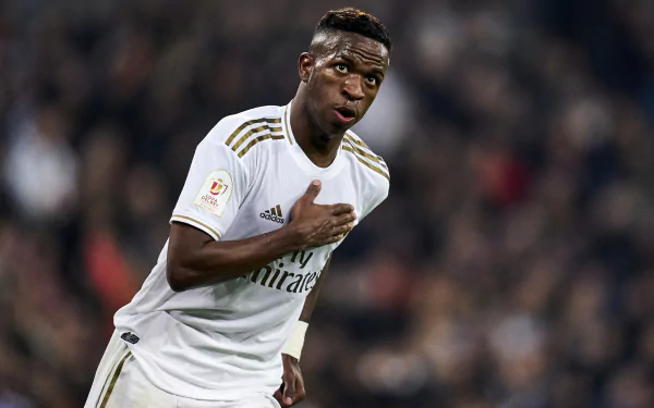 2K Quad HD PC desktop wallpaper showing a professional footballer in a white kit touching his chest during a celebration on a crowded stadium pitch.