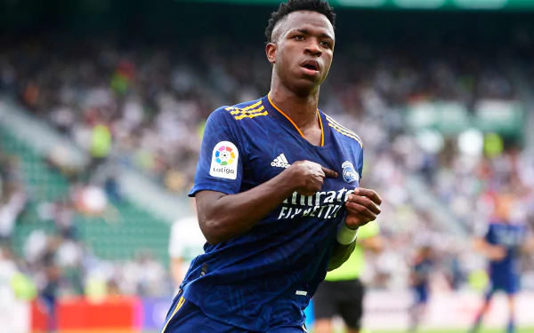 HD PC desktop wallpaper featuring Vinícius Júnior in action, wearing a blue Real Madrid sports jersey on the football field.