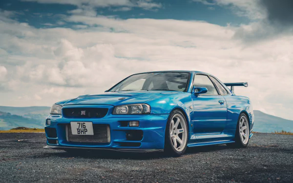 Blue Nissan Skyline R34 displayed as a high-definition wallpaper with a scenic cloudy sky background.