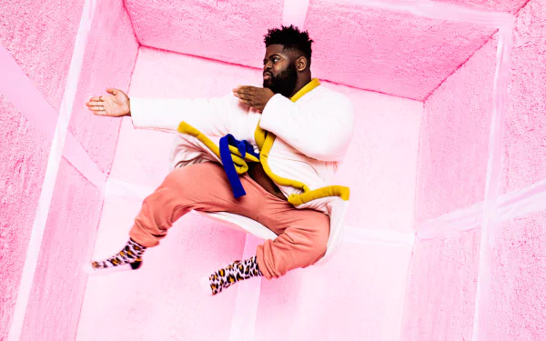 A person in vibrant clothing jumps against a pink geometric background. HD desktop wallpaper with a tag 'Pink Sweats'.