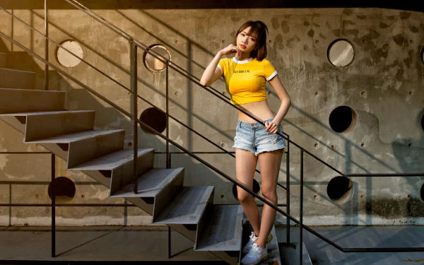 Asian woman wearing shorts and a yellow top poses on an industrial-style staircase with geometric shadows, captured in 4K Ultra HD for a PC desktop wallpaper.