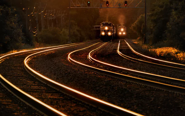 4K Ultra HD PC desktop wallpaper: two train vehicles approach on gleaming curved railroad tracks at dusk, headlights cutting through misty, tree-lined background.