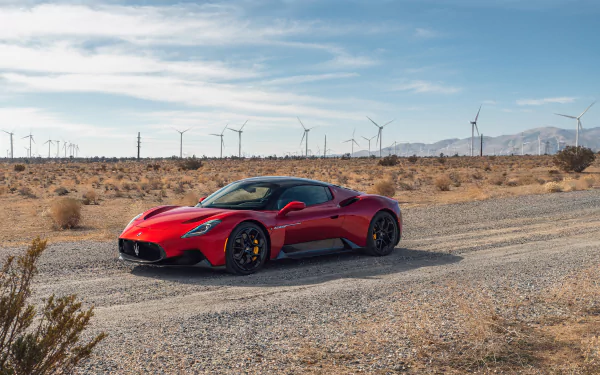 Red Maserati MC20 supercar parked on a desert dirt road with wind turbines and mountains under a blue sky, shown in 4K Ultra HD PC desktop wallpaper quality.