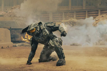 Master Chief from the Halo TV show crouches in battle amid smoke and fire, armored Spartan suit glinting — 2K Quad HD PC desktop wallpaper/background.