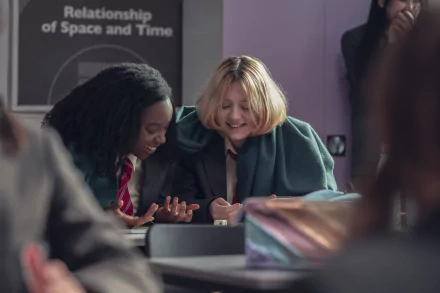 HD PC desktop wallpaper featuring a joyful scene from the TV show Heartstopper, showing two characters sharing a happy moment in a classroom setting.