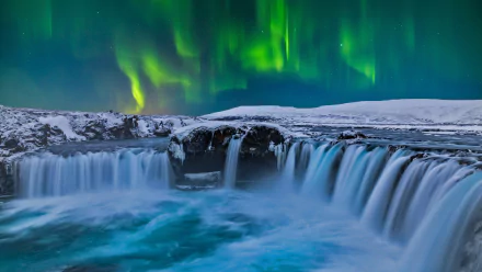 HD desktop wallpaper featuring the stunning Goðafoss waterfall in Iceland, with the vibrant aurora borealis dancing in the night sky. A breathtaking nature scene showcasing the beauty of the Icelandic landscape.