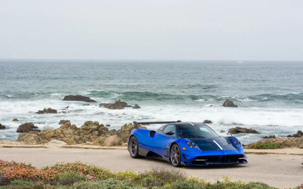 Blue Pagani Huayra sports car parked on a coastal road with rocky shore and waves, HD PC desktop wallpaper/background.