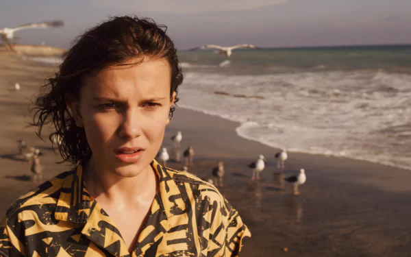 HD PC desktop wallpaper: young woman on a windswept beach, cinematic TV-show portrait with seagulls and rolling waves, moody sci-fi atmosphere.