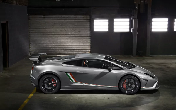 Silver Lamborghini Gallardo vehicle parked in a dim industrial garage, side profile; 8K Ultra HD PC desktop wallpaper/background.