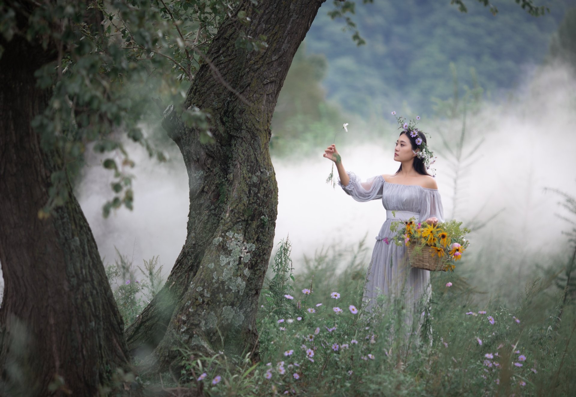 4K Ultra HD wallpaper of an Asian woman in a flowing white dress and flower crown, holding a basket of sunflowers, standing in a misty forest clearing.