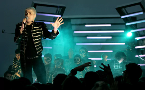 2K Quad HD PC wallpaper: punk‑rock vocalist in a military jacket fronting a theatrical band with skull makeup, green stage lights and a silhouetted, cheering crowd during a live music set.