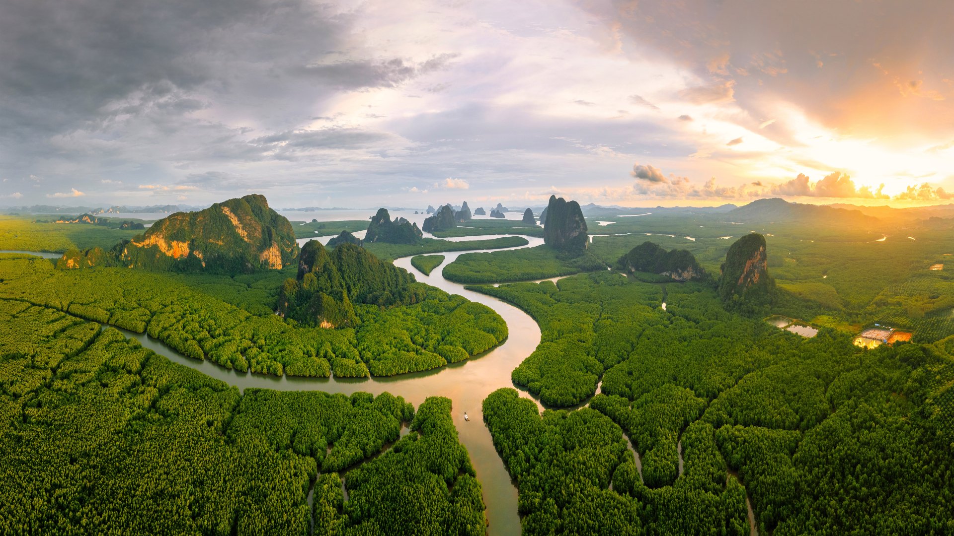 A stunning 4K Ultra HD landscape of Phang Nga Bay, Thailand, showcasing lush mangroves winding around limestone karsts under a dramatic sky at sunrise.