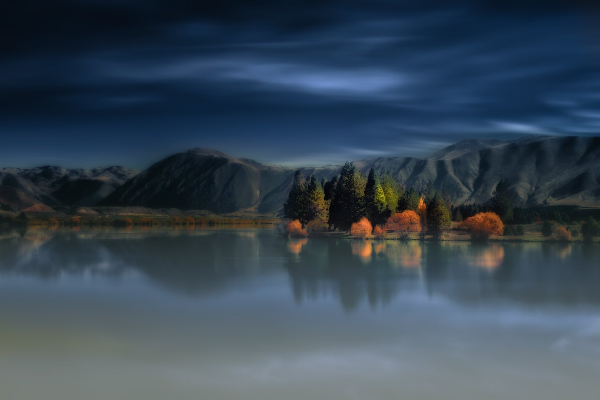 HD PC desktop wallpaper background: tranquil nature scene — mountain lake at dusk with a small illuminated island of trees and crisp reflections beneath moody clouds.