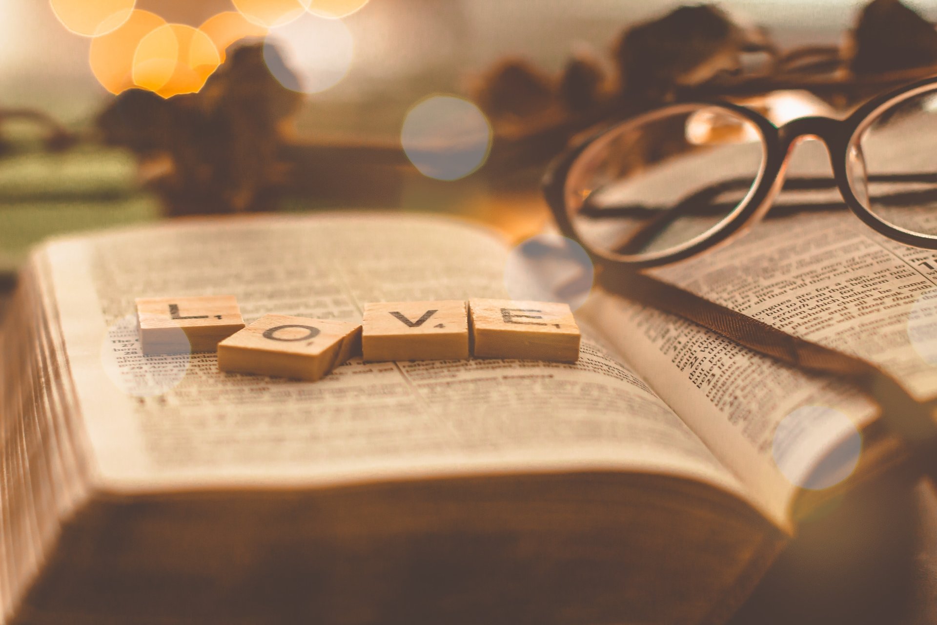 A warm, softly lit 4K Ultra HD photography wallpaper showing wooden letter tiles spelling LOVE on an open book, with glasses resting beside it.