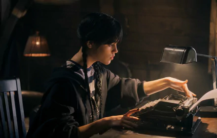 Jenna Ortega as Wednesday Addams from the TV show Wednesday types on a vintage typewriter in a dimly lit room, featured in an HD PC desktop wallpaper.