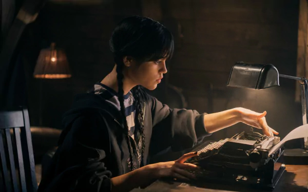 Jenna Ortega as Wednesday Addams from the TV show Wednesday types on a vintage typewriter in a dimly lit room, featured in an HD PC desktop wallpaper.