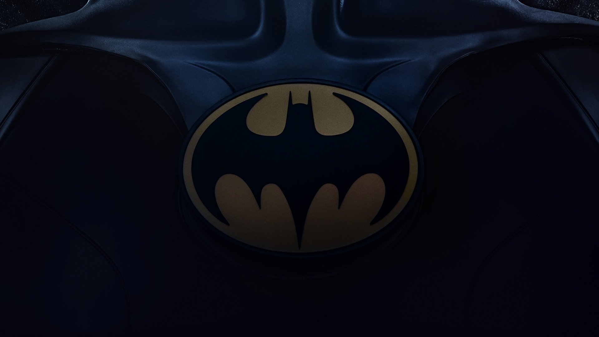 2K Quad HD PC desktop wallpaper: moody close-up of Batman emblem on armored chest, dark blue lighting — movie still from The Flash (2023).