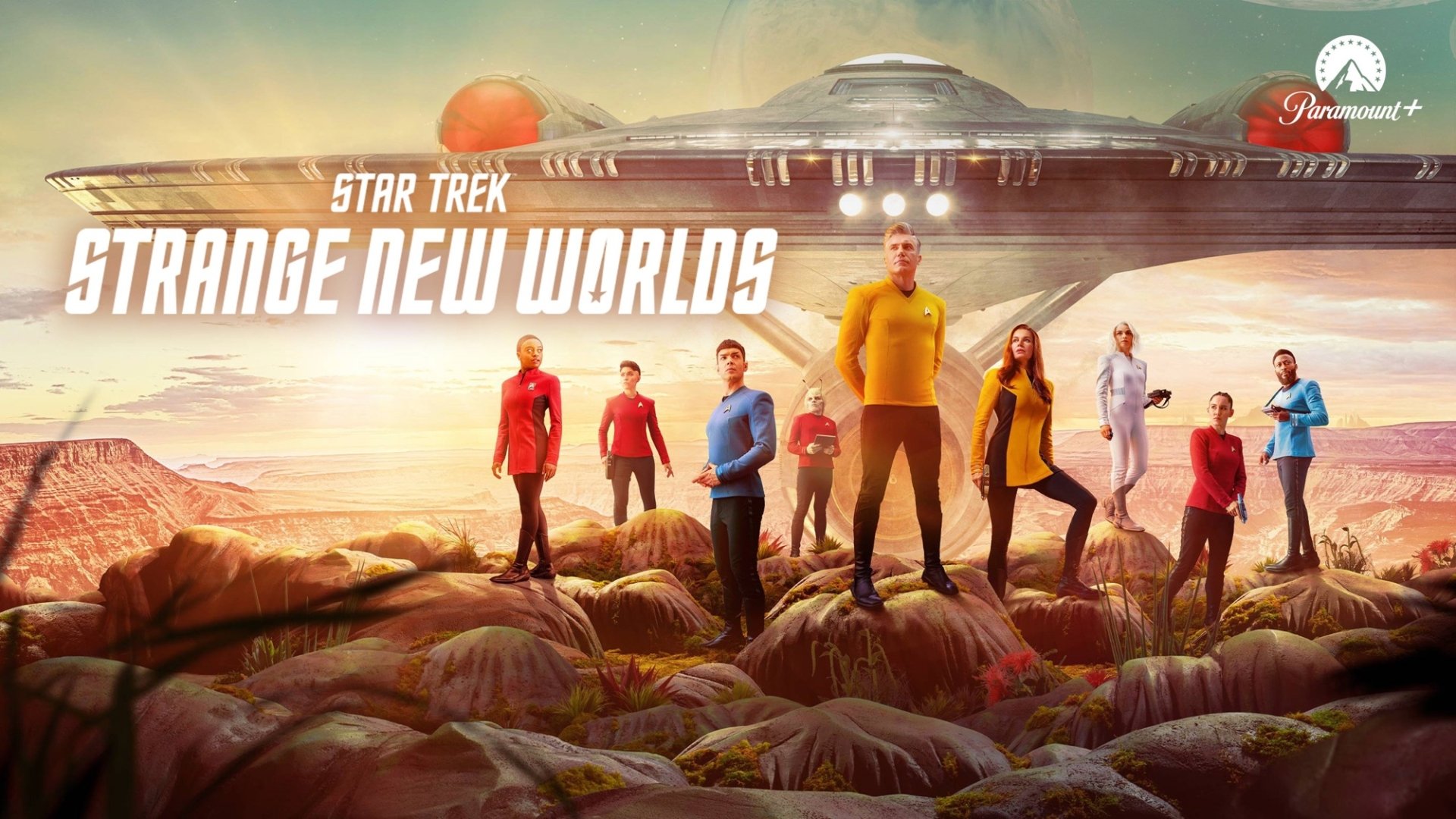 HD PC desktop wallpaper background of TV show Star Trek: Strange New Worlds — the USS Enterprise looms over a rocky alien plain while the crew in colorful Starfleet uniforms stand posed.