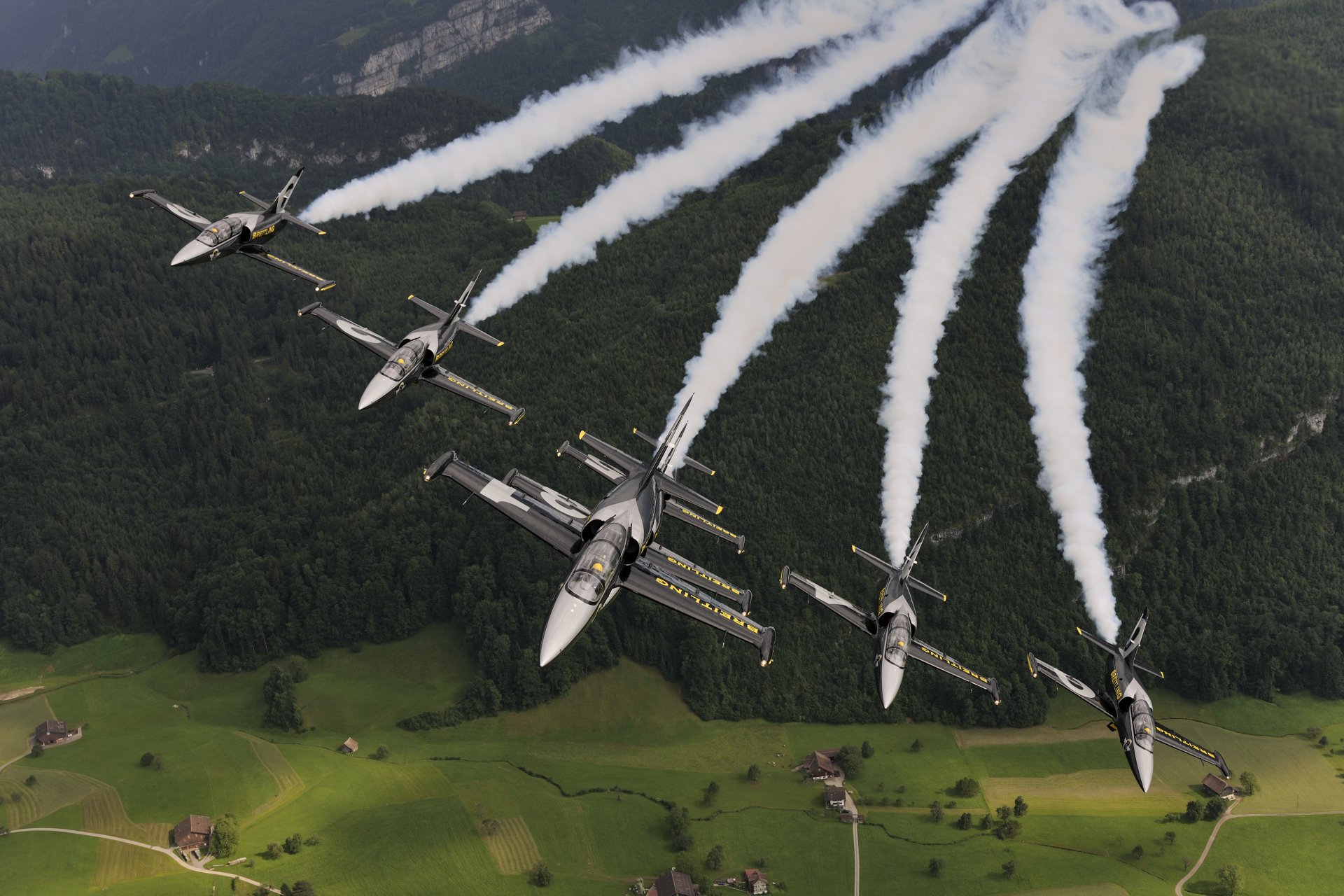 A formation of Aero L-39 Albatros military jets releases white smoke trails over green fields, captured in vibrant 4K Ultra HD for a dynamic desktop wallpaper.