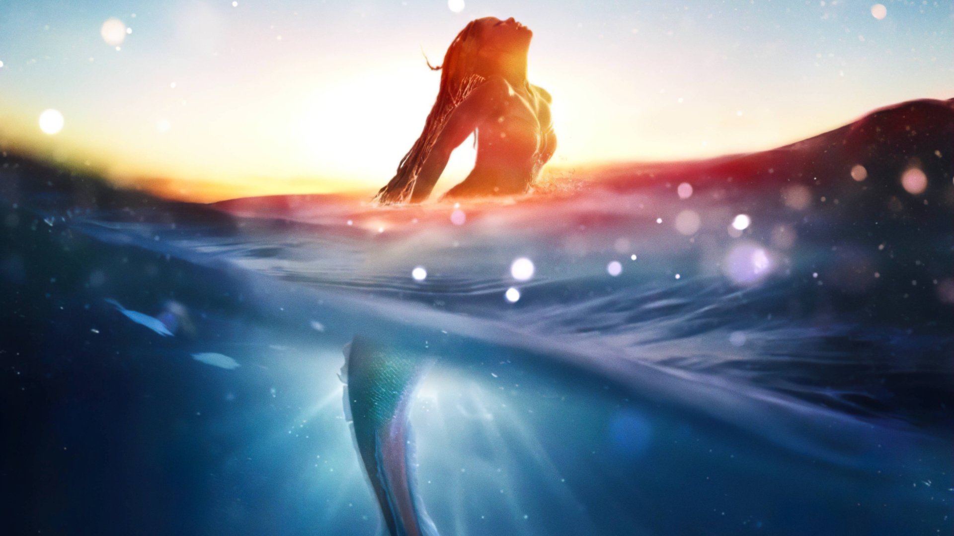 A 4K Ultra HD PC desktop wallpaper of Ariel, the mermaid from The Little Mermaid (2023), emerging from the water at sunset with shimmering light reflections.