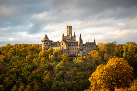 A 4K Ultra HD wallpaper featuring the man-made Marienburg Castle in Hanover, surrounded by autumn-colored trees under a cloudy sky.