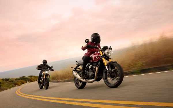 A Triumph Speed 400 motorcycle rides along a winding road, accompanied by another bike, set against a vibrant sunset in this stunning 8K Ultra HD desktop wallpaper.