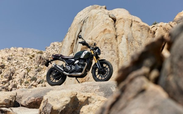 HD desktop wallpaper featuring a Triumph Scrambler 400 X motorcycle parked on a rocky desert terrain, highlighting the bike's rugged design suitable for outdoor backgrounds.