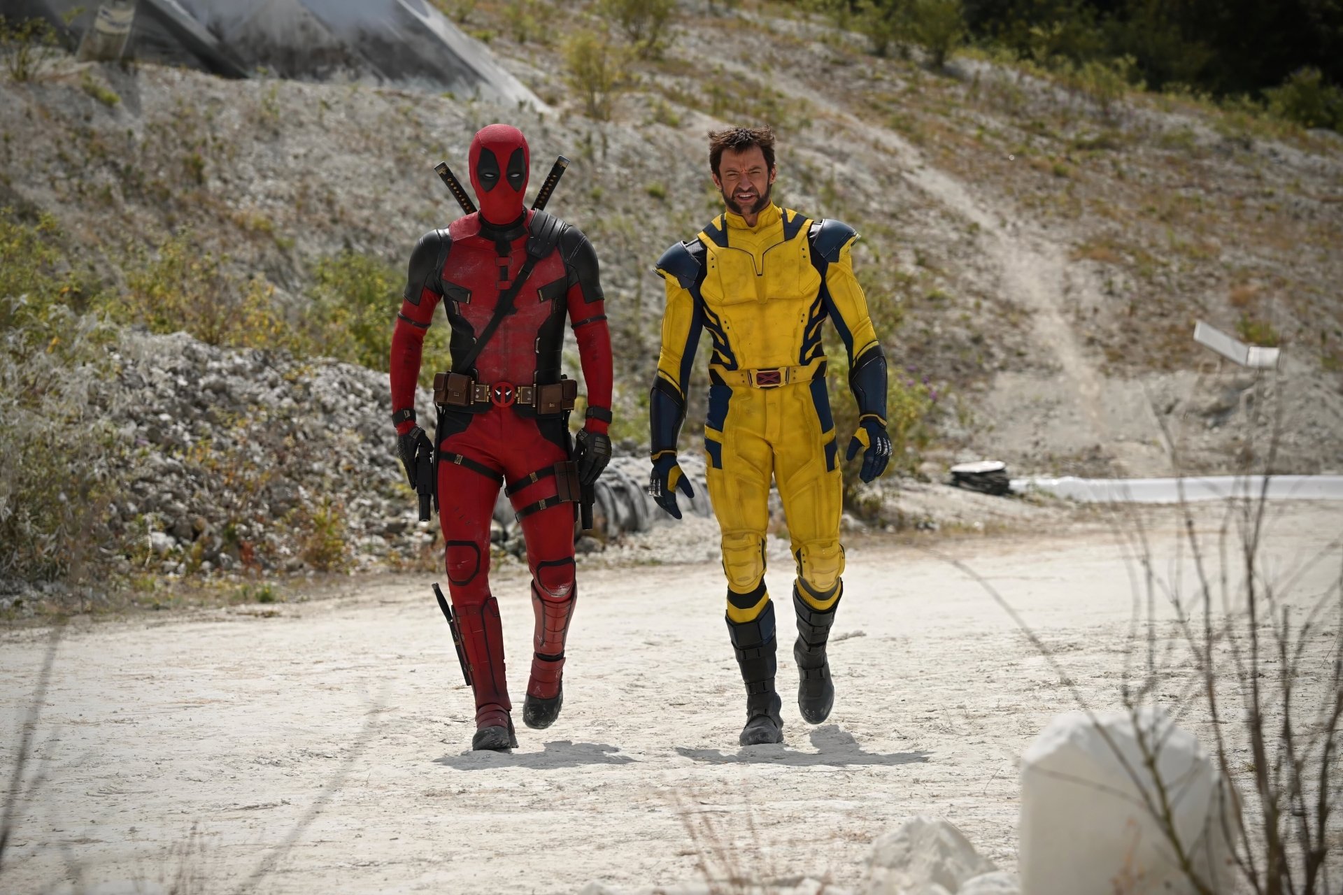 Deadpool and Wolverine, portrayed by Hugh Jackman, walk together in this dynamic HD wallpaper from the movie Deadpool & Wolverine. A striking scene set against a rugged backdrop.