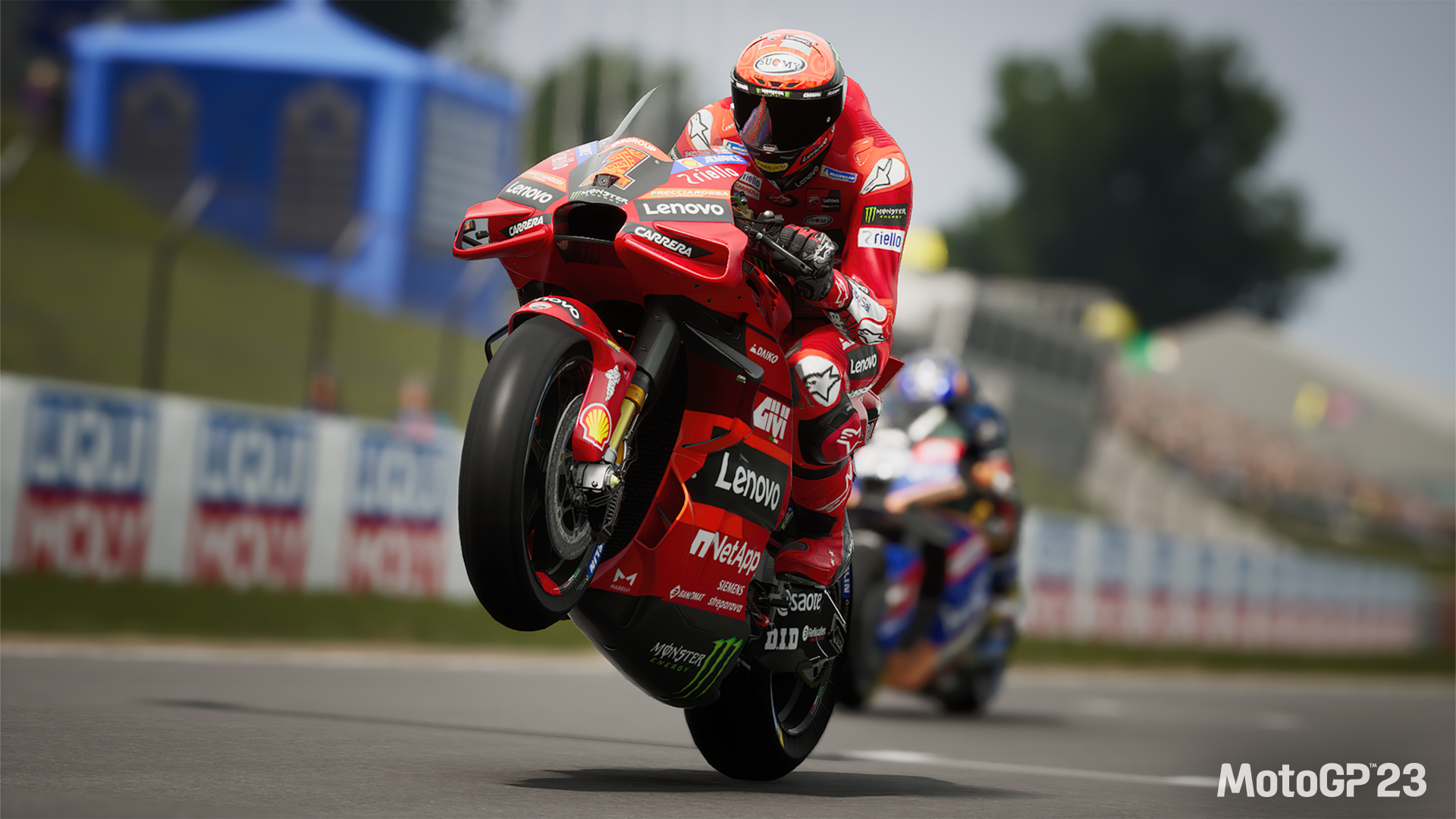 HD desktop wallpaper of a MotoGP 23 video game scene featuring a motorcyclist performing a wheelie on a race track.