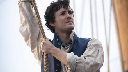 A close-up of Prince Eric from The Little Mermaid (2023), showcasing his determined expression as he holds onto a rope aboard a ship, set against a beautiful ocean backdrop.