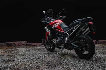 HD desktop wallpaper featuring the Triumph Tiger 900 GT Aragón motorcycle, poised on a gritty surface with a dark backdrop, showcasing its sleek red and black design.