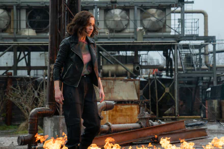 Emilia Clarke in a dramatic scene from Secret Invasion as an HD desktop wallpaper with industrial backdrop and fire elements.