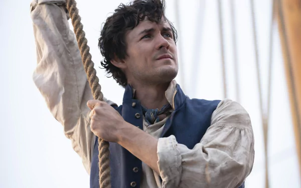 A close-up of Prince Eric from The Little Mermaid (2023), showcasing his determined expression as he holds onto a rope aboard a ship, set against a beautiful ocean backdrop.