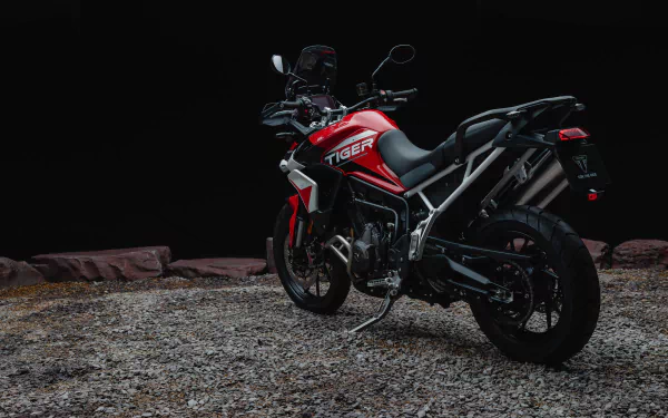 HD desktop wallpaper featuring the Triumph Tiger 900 GT Aragón motorcycle, poised on a gritty surface with a dark backdrop, showcasing its sleek red and black design.