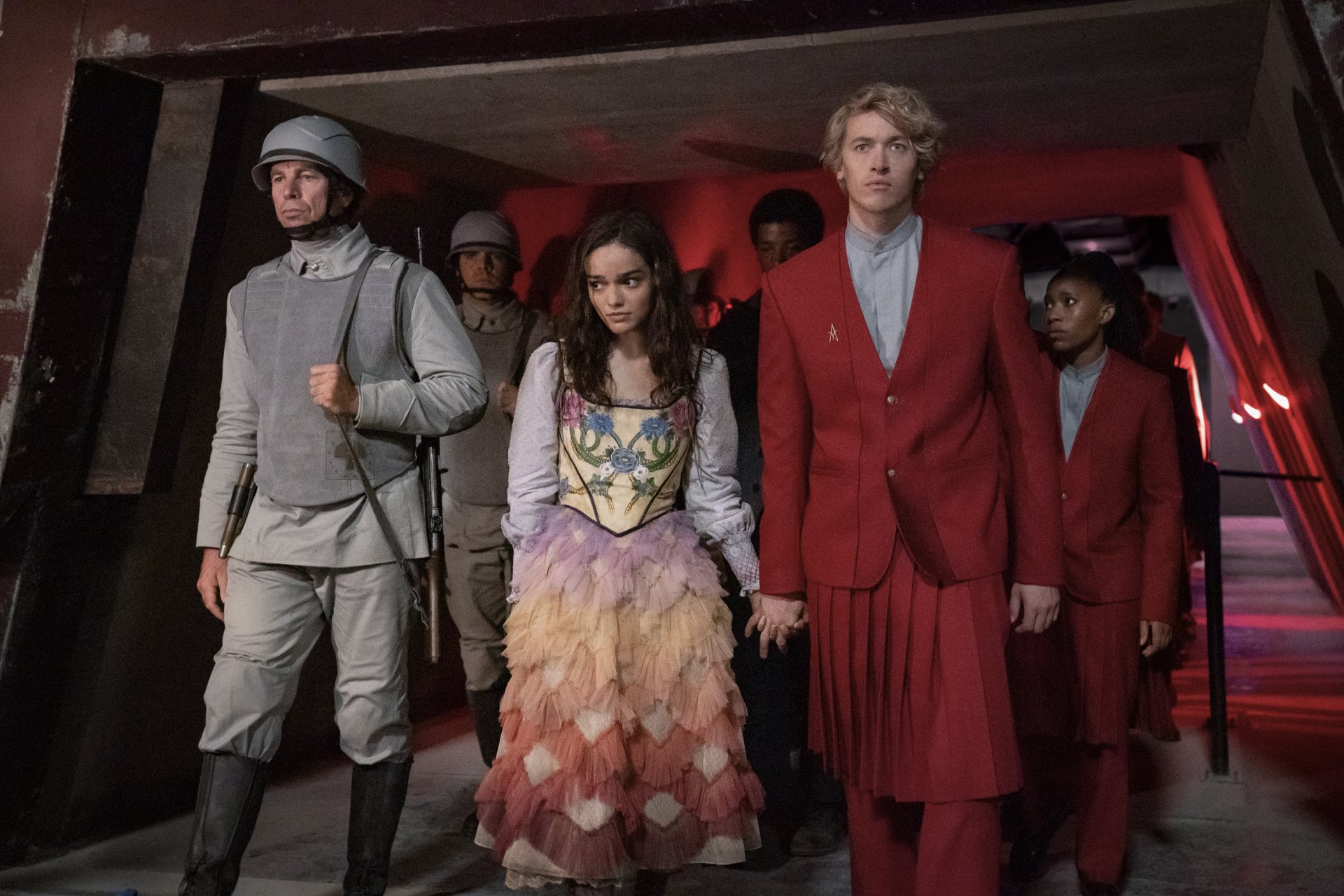 A scene from The Hunger Games: The Ballad of Songbirds & Snakes, featuring characters in vibrant costumes walking through a dimly lit corridor, creating a striking HD desktop wallpaper.