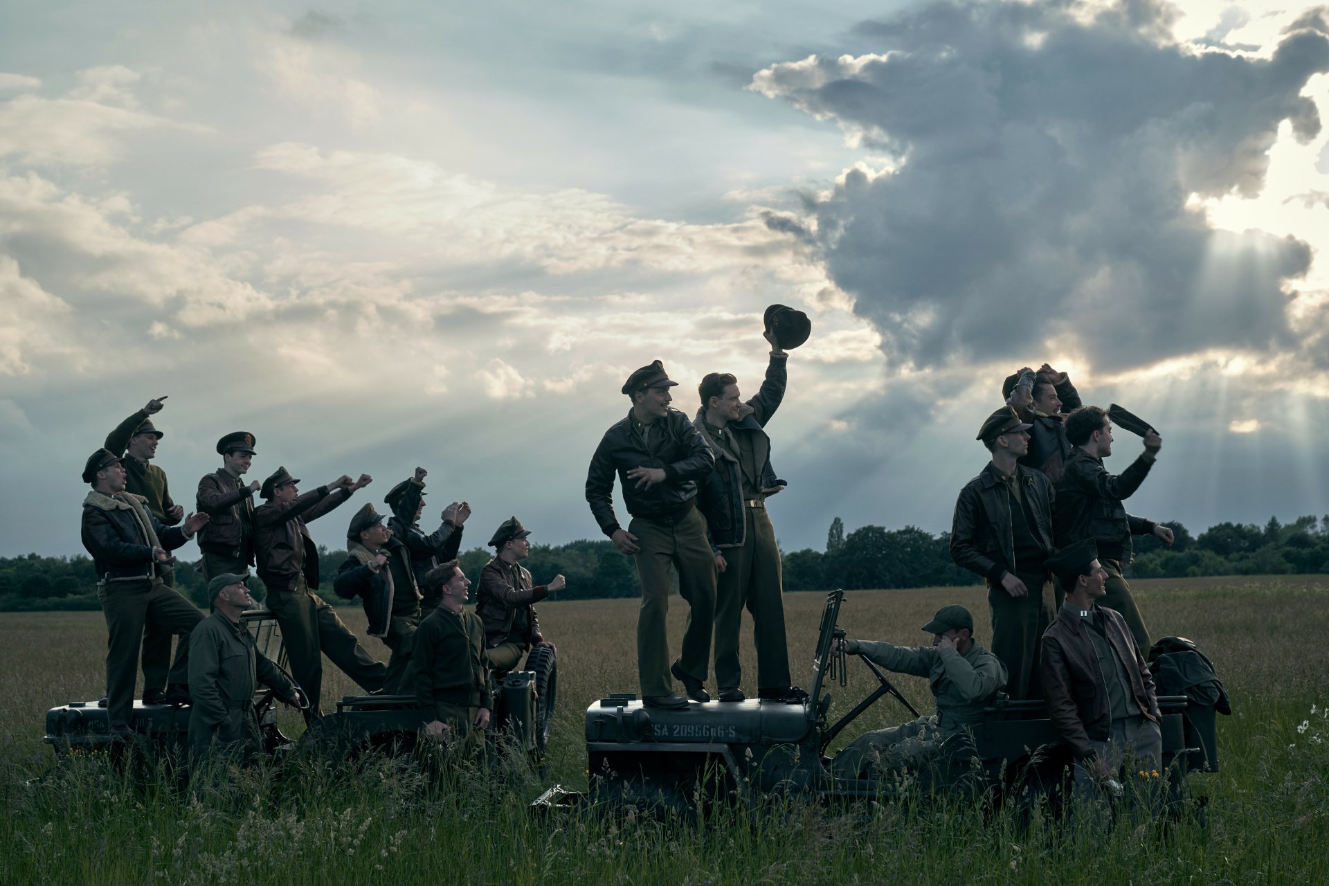 Group of military personnel in period uniforms gazing skyward against a dramatic cloud-filled sky in a high-definition 'Masters of the Air' TV show desktop wallpaper.