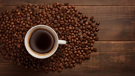 HD wallpaper featuring a cup of coffee surrounded by coffee beans on a wooden surface.