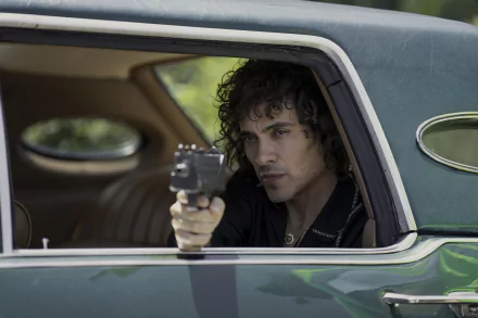 A tense scene from the TV show *Griselda* (2024), featuring a character aiming a gun from the window of a vintage car, captured in high-definition wallpaper.